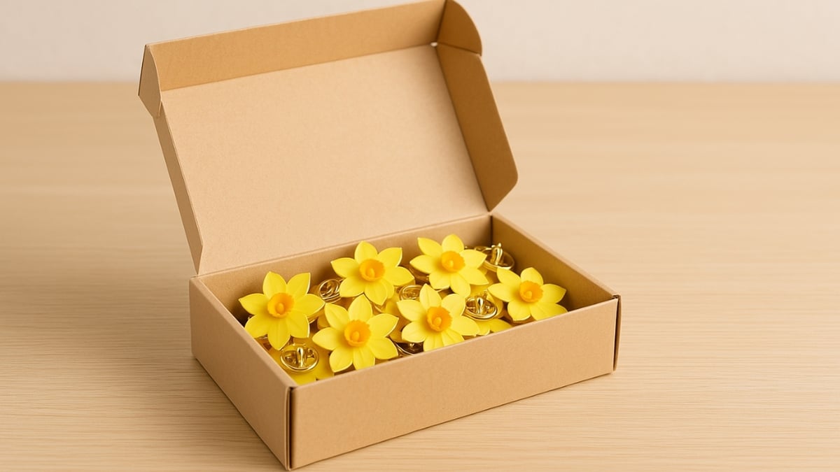 Open cardboard box filled with yellow daffodil awareness pins on a wooden surface