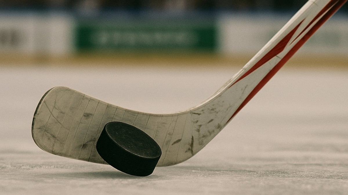 A close-up view of a hockey stick positioned behind a black puck on the ice rink.