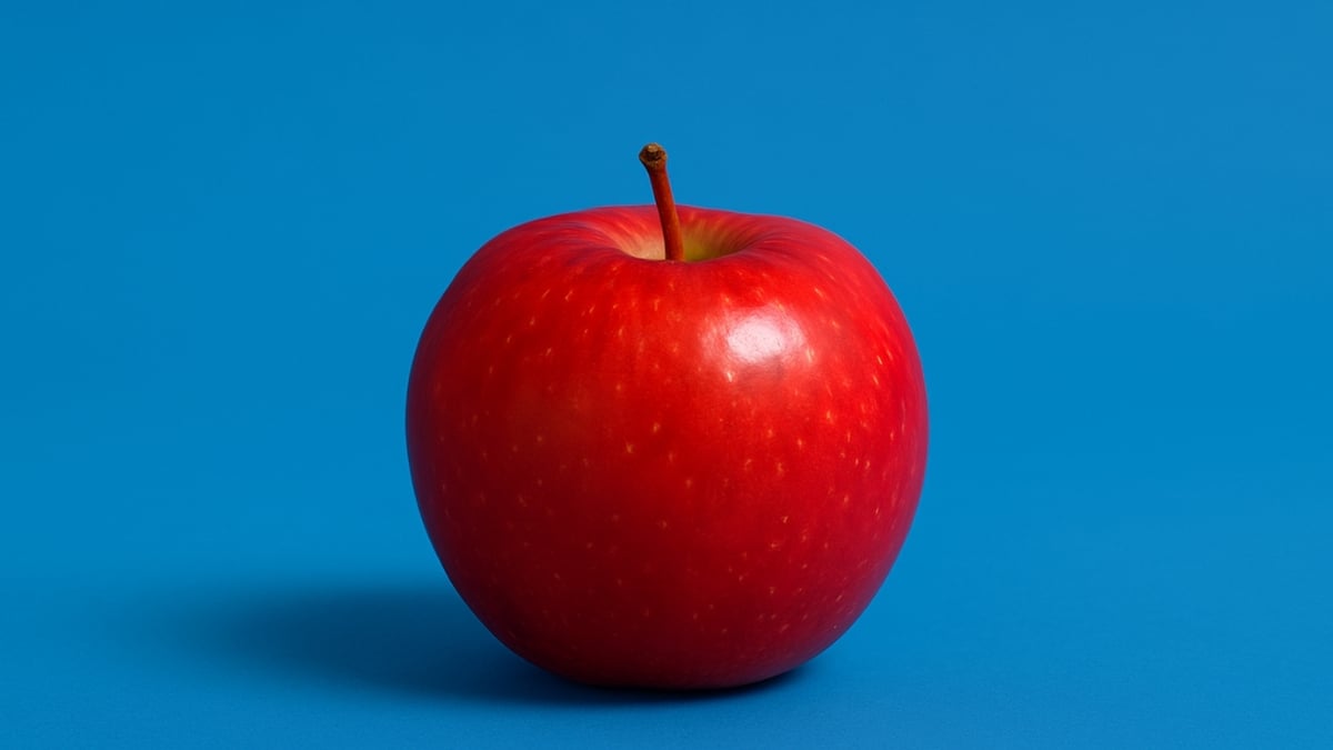 A single red apple with a stem placed on a bright blue background with a soft shadow.
