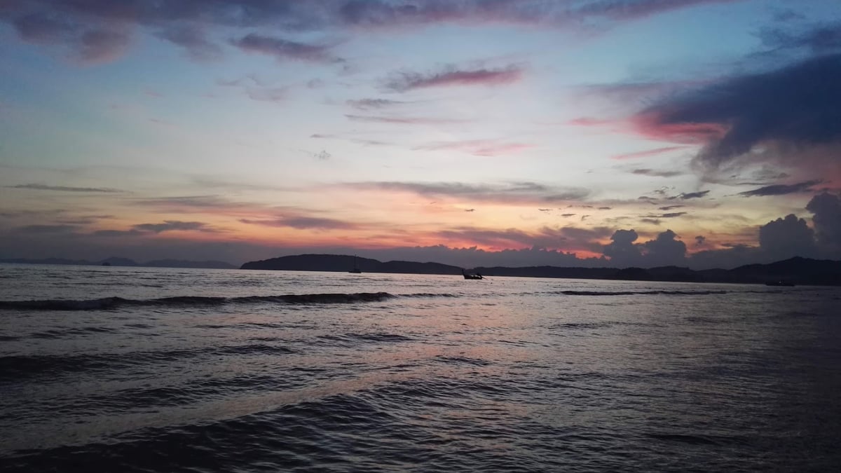 Waves ripple across the sea under a vibrant sunset sky with distant islands.