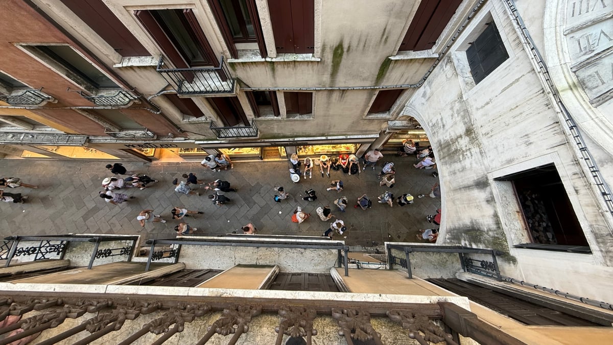 People walking and gathering along a narrow Venetian street seen from a high vantage point.