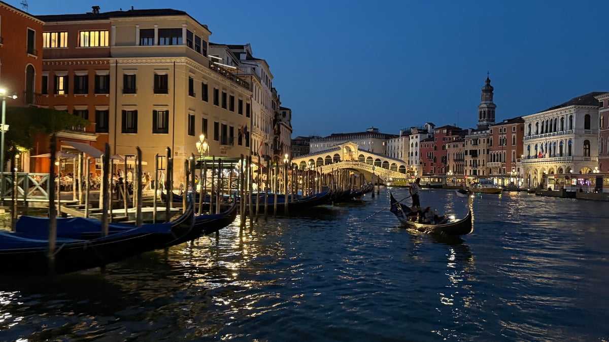 Gondolas floating on Venice's Grand Canal near the illuminated Rialto Bridge at night.