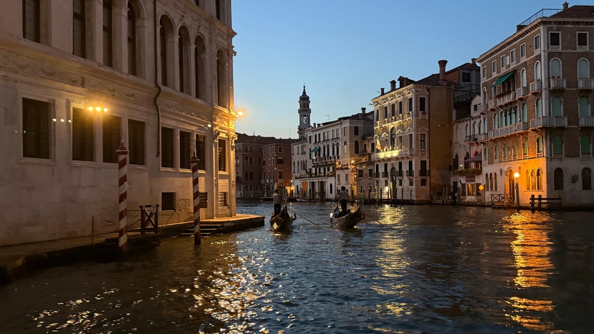 Two gondolas gliding on Venice's Grand Canal at dusk with softly lit historic buildings.