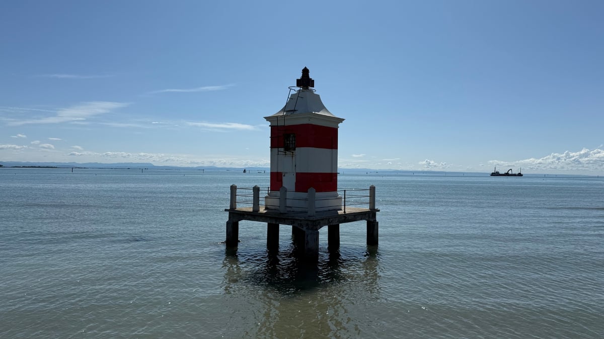 A red and white lighthouse standing on pillars in calm sea waters under a clear blue sky.