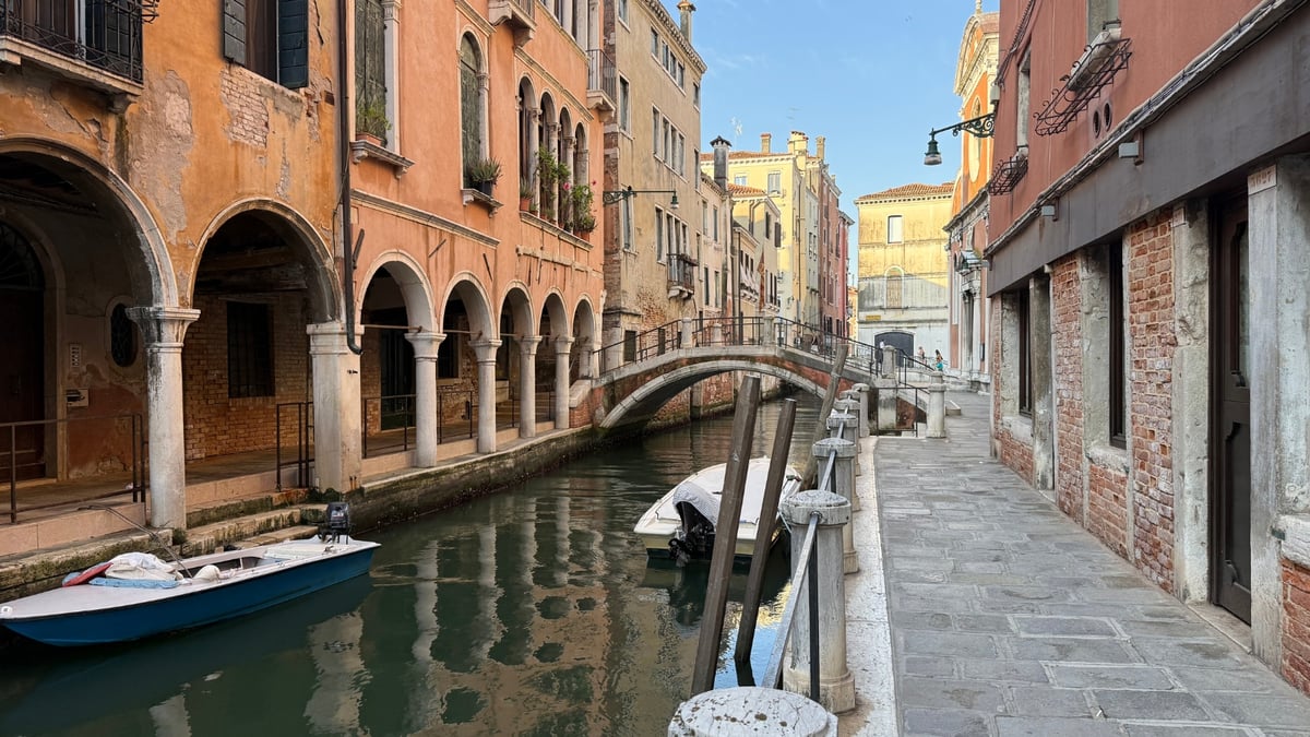 A Venetian canal with small boats and an elegant arched stone bridge lined by colorful historic buildings.