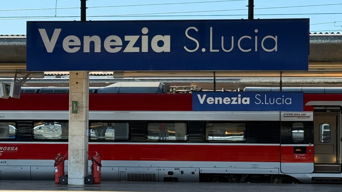 Two blue Venezia S. Lucia signs hang above a red and white high-speed train with visible windows and doors.