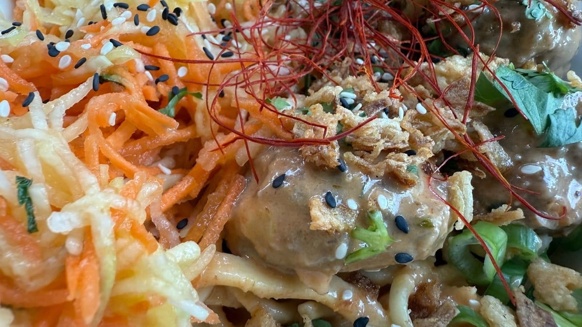Meatballs with noodles, creamy sauce, shredded vegetables, sesame seeds, and herbs.