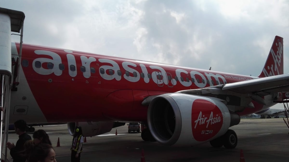 AirAsia Airbus parked at the airport gate with passengers boarding under a cloudy sky.