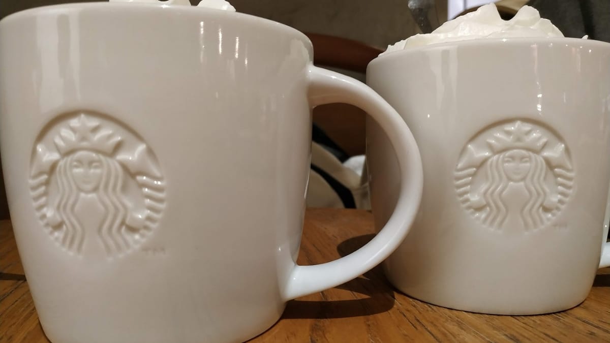 Two white ceramic mugs filled with coffee and topped with whipped cream, placed on a wooden table in a cozy café.