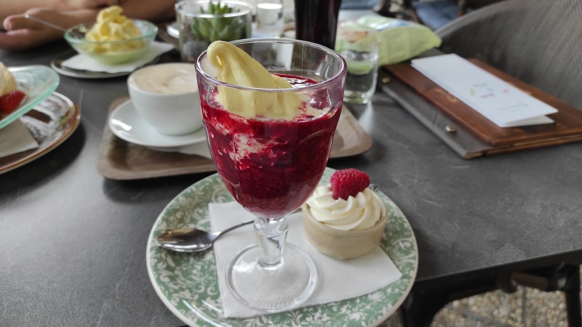 A raspberry dessert with vanilla ice cream served in a glass, accompanied by a small whipped cream pastry in a café setting.