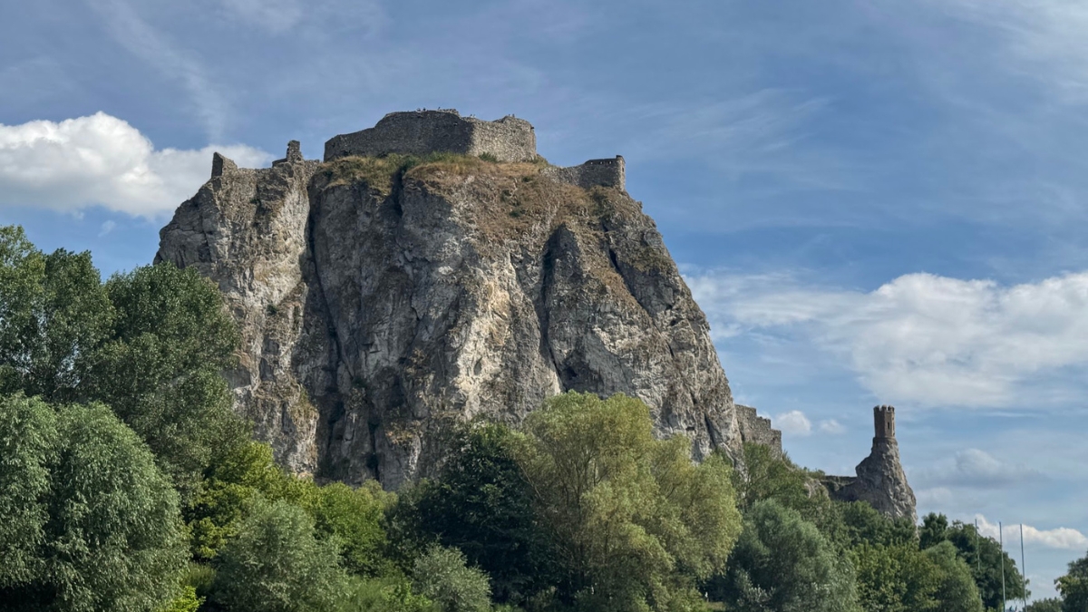 Stone ruins of Devín Castle on a high cliff above the Danube River with trees and blue sky in the background