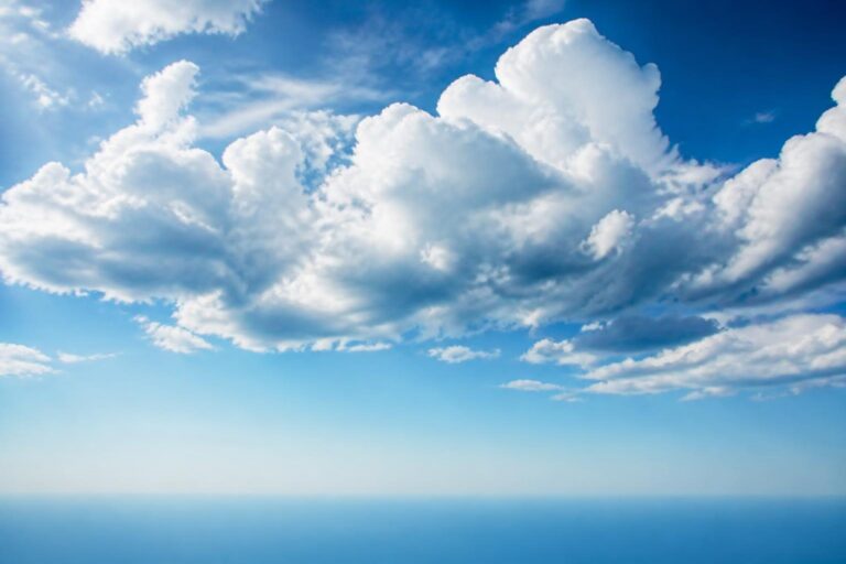 Clear blue sky with large white fluffy clouds over a distant horizon
