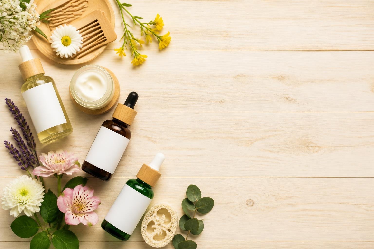 Natural skincare bottles and cream jar with fresh flowers on light wood surface