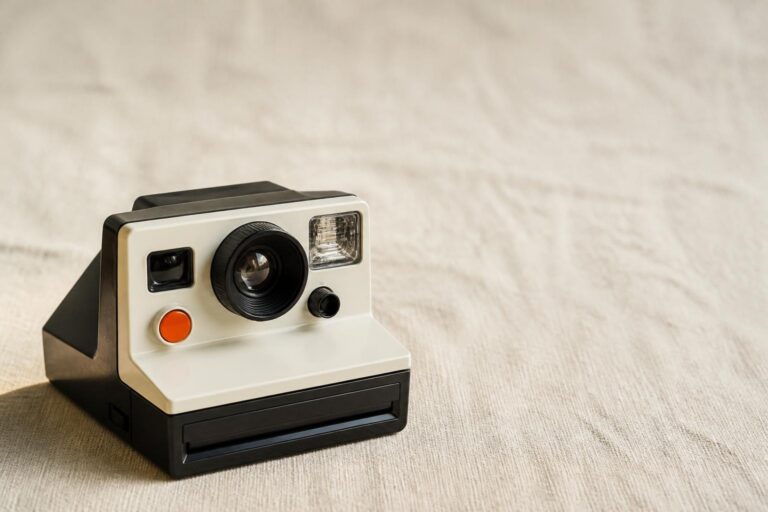 Black and white retro instant film camera with orange button on beige fabric